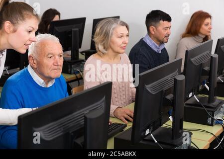 Computer lessons for adults. Group of senior people learning to use computers with young female tutor in classroom Stock Photo