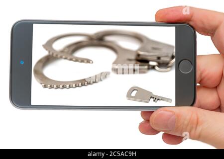 Metal handcuffs on smartphone screen. The detention of criminals breaking the law. Restriction of freedom. Stock Photo