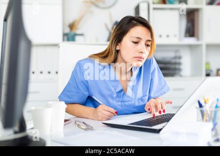 Young hispanic woman doctor assistant working in medical office using laptop computer Stock Photo