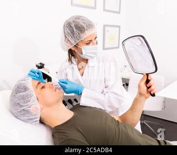 Young man client and woman cosmetologist examining face skin for cosmetology beauty treatment at esthetic clinic Stock Photo