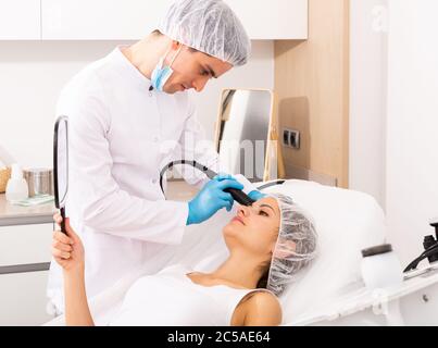 Young woman receiving face rejuvenation treatment on modern equipment at cosmetology clinic Stock Photo