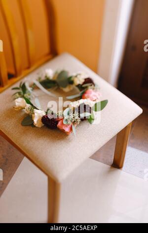 brides wreath of white and pink roses, branches of eucalypt tree and burgundy chrysanthemum with thin ribbons on a textile beige chair Stock Photo