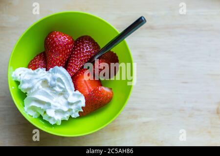 Fresh from the garden. Strawberries and cream in a green bowl with a spoon Stock Photo