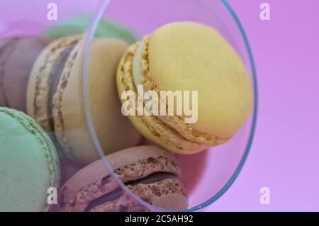 Macarons of various colors and flavors in a glass cup with light pink background Stock Photo