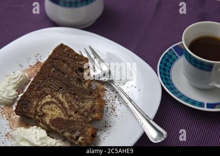 A plate with a slice of zebra or tiger tart, some whipped cream and a cup of coffee on a purple surface Stock Photo
