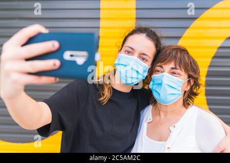 Mother and daughter making a selfie in the street protected by a mask. Family protected with a mask. Family selfie with mask. Selfie with mask. Human Stock Photo