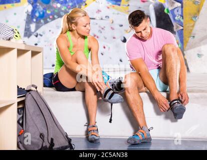 Smiling cheerful pair of sports people dressing for mountaineering outfit for climbing on artificial rock wall indoors Stock Photo