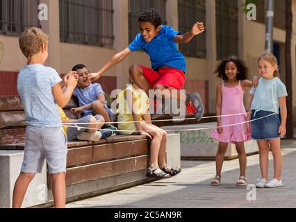 Mexican boy playing rubber band jumping game with european friends and laughing outdoor Stock Photo