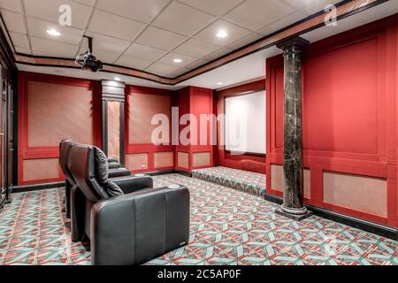 A large, red home theater with dark seating, a large screen, and projector. Stock Photo