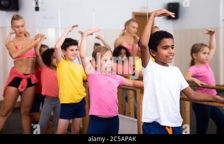 Focused children standing along ballet bar in dance studio during class Stock Photo