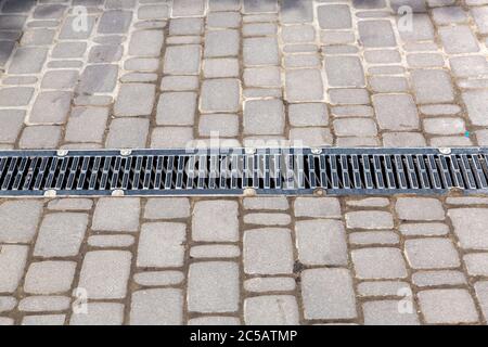 A lattice of a drainage paving system on a path made of square stone tiles, close up. Stock Photo