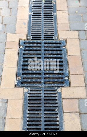 A lattice of a drainage paving system with hatch grill on a walkpath made of stone tiles, close up. Stock Photo