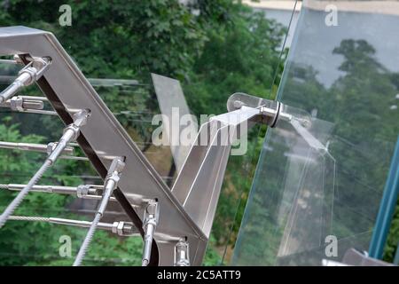 a corner of a glass bridge with tension steel cables and a cable tensioner with thread close up. Stock Photo