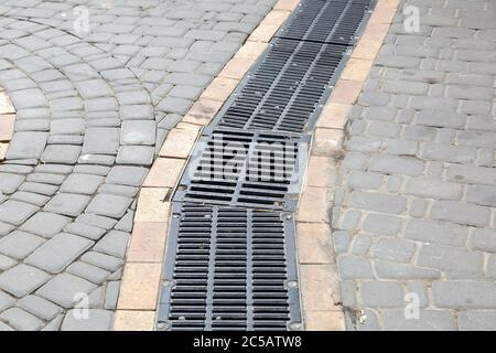 A lattice of a drainage paving system with hatch grill on a curve path made of stone tiles, close up. Stock Photo