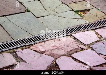 A lattice of a drainage paving system on a walkway made of cobblestone tiles, close up of a rainwater drainage system, nobody. Stock Photo