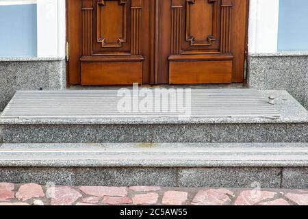 gray granite threshold with steps covered with non-slip rubber strips at the entrance wooden door of brown color at the facade of the building, front Stock Photo