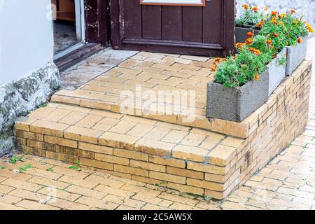brick threshold with a step at the open wooden entrance door with gray stone flowerpots for flowers, a closeup of architectural details. Stock Photo