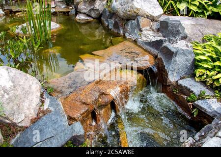 waterfall on stone artificial pond with flow water in the park on a day, closeup. Stock Photo