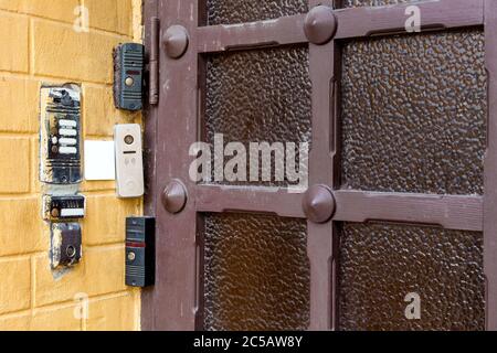 several intercoms and electronic locks on a chip or card on brick wall on outdoors against a wooden door with glass, closeup remote security control t Stock Photo