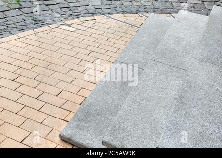 Granite stone steps descent to the pedestrian sidewalk of the old city from stone tiles, close-up. Stock Photo