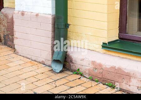 green rain pipe rain system on the facade of the brick house near the stone sidewalk, close up of an architectural element. Stock Photo