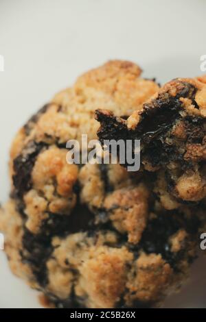 Vertical closeup of a chocolate chunk on top of a dark chocolate oatmeal cookie on white background Stock Photo