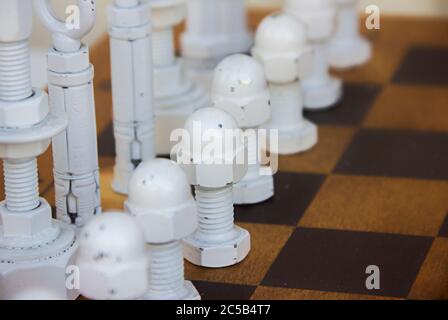 painted white screws, dowels, hooks, clamps, holders and fasteners and other small ironware on a chessboard used as chess pieces, concept of man pawn Stock Photo