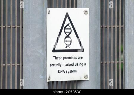 Black and white sign on a metal fence with DNA symbol reads these premises are security marked using a DNA system, England UK Stock Photo