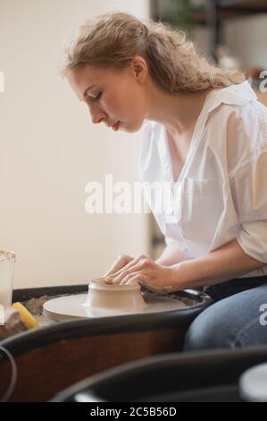 Female potter working with clay on wheel in studio. Clay with water splattered around the potter wheel. Stock Photo