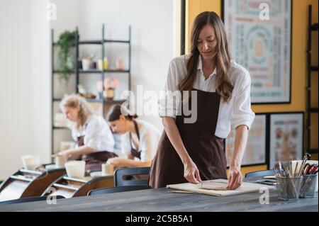 Close up of skilled craftswoman removing part of clay while making ceramic product in pottery workshop Stock Photo