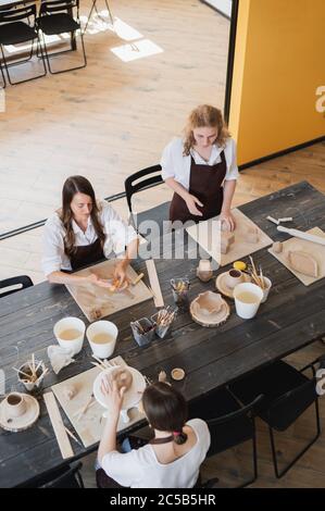 In the clay workshop. Female potters talking and smiling during the working process in the clay workshop. Female potter masters rolling up the clay on Stock Photo