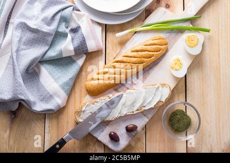 Freshly baked bread bun cut in halves and prepared as a simple sandwich of soft cheese, eggs and herbs Stock Photo