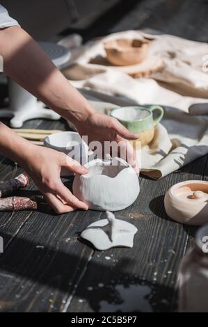 Female hands gently putting the finished glazed bowl on a wooden table with different pottery tools. Stock Photo