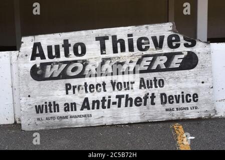 A battered sign in a parking lot in British Columbia, Canada warns drivers that theft from cars is a problem in the lot. Stock Photo