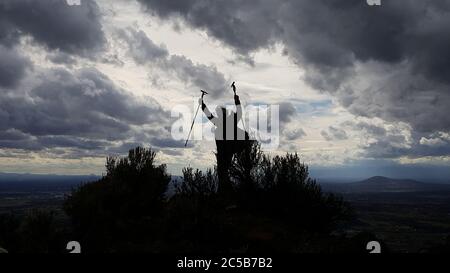 The silhouette of a male hiker celebrating reaching the summit as a storm moves in. Stock Photo