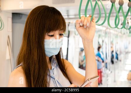Young Asian woman passenger wearing surgical mask and listening music via mobile phone in subway train Stock Photo