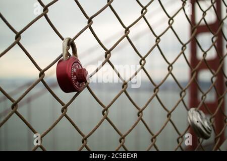 Love locks on Golden Gate Bridge, San Francisco, California. Red combination lock & round padlock. Northern tower of iconic bridge in background. Stock Photo