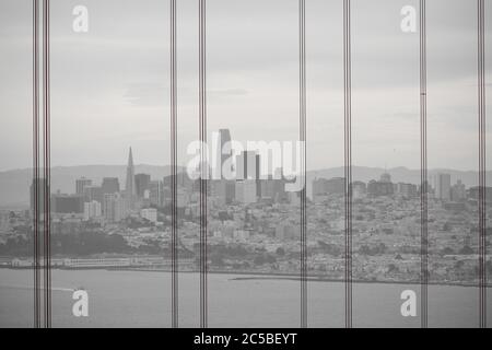 Hazy view of San Francisco from Golden Gate Bridge with bridge cables in the foreground. Embarcadero Center, Salesforce Tower, Transamerica Pyramid. Stock Photo