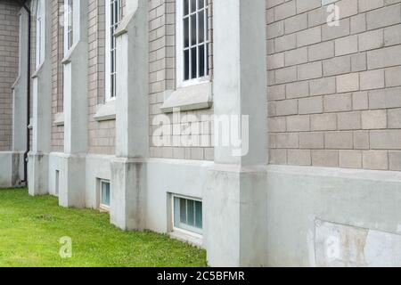 The exterior wall of a large tall vintage building made of beige bricks, grey concrete and multi pane closed glass white windows. Stock Photo