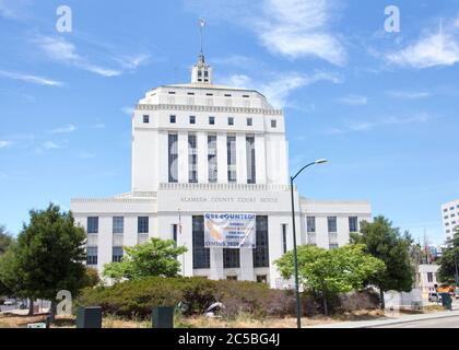 Oakland, CA - June 20: 2020: Alameda County Court house with Census 2020 sign hanging on the front. Tents in homeless encampment tucked into the bushe Stock Photo