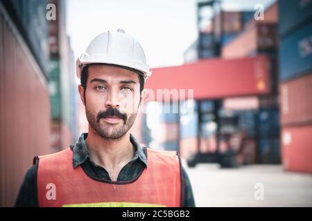 Portrait of Confident Transport Engineer Man in Safety Equipment Standing in Container Ship Yard. Transportation Engineering Management and Container Stock Photo