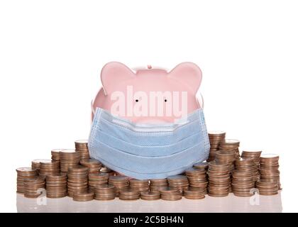 Pink traditional piggy bank wearing a surgical mask sitting on a reflective surface with piles of quarters next to it. Pandemic savings Stock Photo