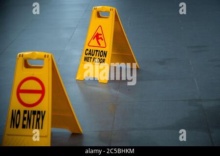 Yellow wet floor caution and no entry sign during rain with puddle of water when floor is slippery and copy space for text Stock Photo