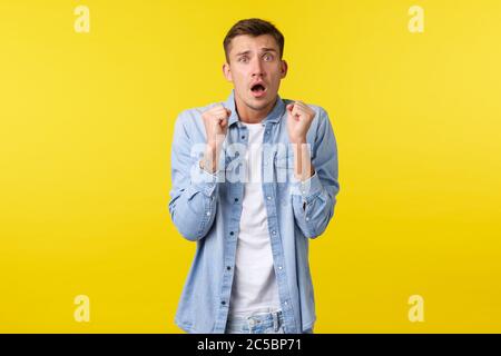 Scared timid guy trembling from fear, looking worried and nervous, shivering and staring concerned camera, raising fists up clumsy. Weak man trying Stock Photo