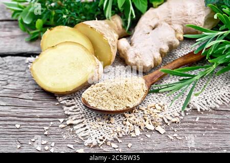 Ground ginger in a spoon, flakes and ginger root on burlap, spicy herbs on a background of an old wooden board Stock Photo