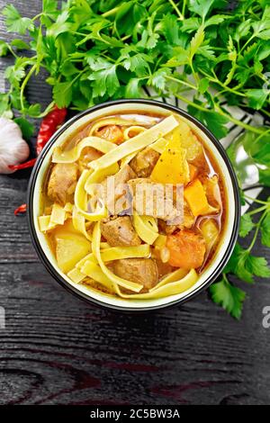 Central Asian national dish Lagman of meat, noodles and vegetables in bowl on a napkin, garlic, parsley on wooden board background from above Stock Photo