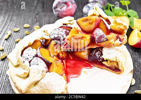 Sweet pie with plum, sugar and cardamom on paper, sprigs of green mint on a dark wooden board background Stock Photo