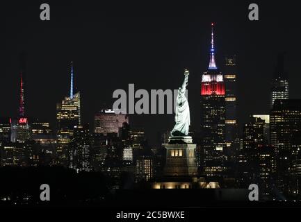 Bayonne, United States. 01st July, 2020. The Statue of Liberty stands to the left of the Empire State Building which is lit up in red, white and blue before a Macy's Fourth of July fireworks show takes place in Times Square on Wednesday, July 1, 2020 in Bayonne, New Jersey. New York City prepares to enter phase 3 of a four-part reopening plan on July 6 after being closed for almost 4 months due to COVID-19. Photo by John Angelillo/UPI Credit: UPI/Alamy Live News