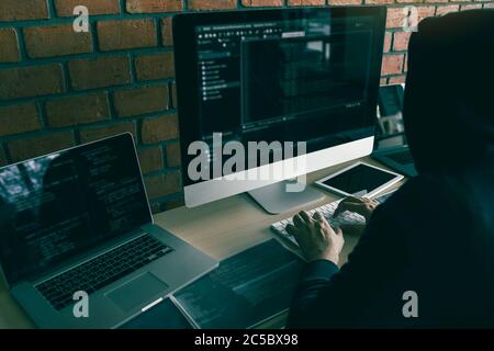 Hacker in the hood working with computer with hacking breaking into data servers. Stock Photo