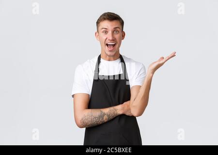 Small business owners, coffee shop and staff concept. Relieved and happy smiling handsome barista rejoicing, raise hand and looking excited, telling Stock Photo